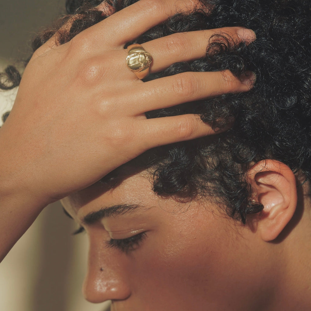 Person with hand on head wearing a gold ring, close-up
