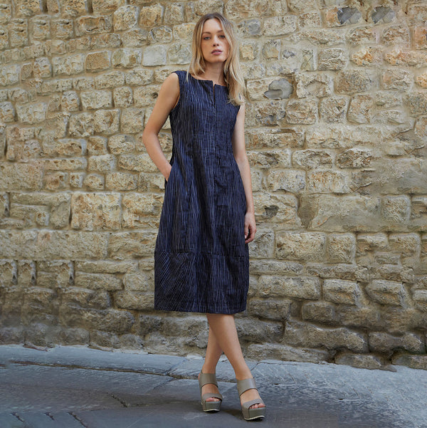 Model wearing a navy blue and white striped tapered dress with a split neckline. Her right is placed inside one of the included pockets.
