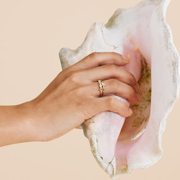 Hand holding a large shell with a gold ring on a beige background