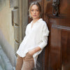 Woman posing wearing a buttoned white, 3/4 long sleeve collared top.