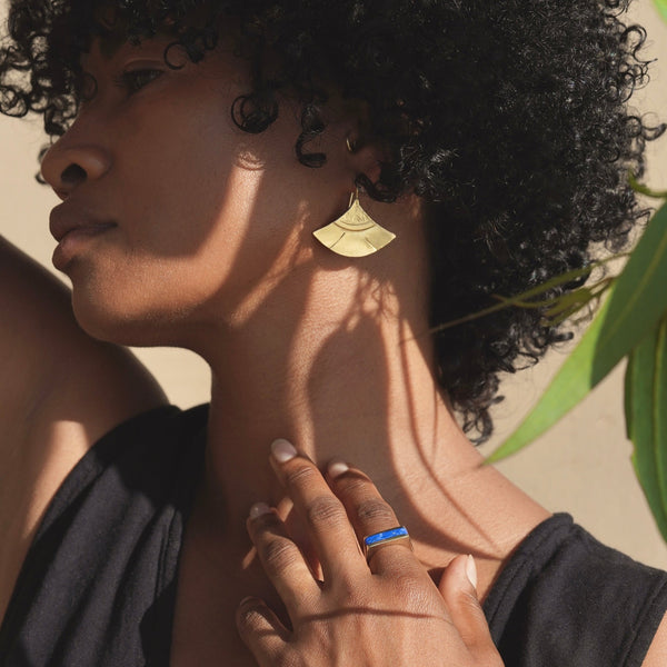 Woman wearing a gold earring and blue ring with a blurred background