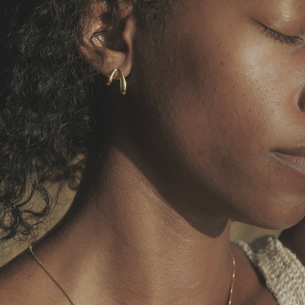 Close-up of a person wearing gold jewelry including earrings and a necklace.