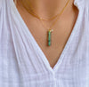 Gold necklace with a green pendant on a white shirt