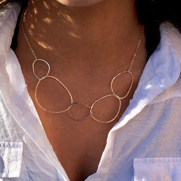 Gold necklace with interlocking rings worn by a person in a white shirt.
