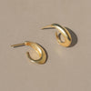 A pair of gold vermeil huggie studs that begin thicker on the end attached to the post, and ends with a thinner point at the end.