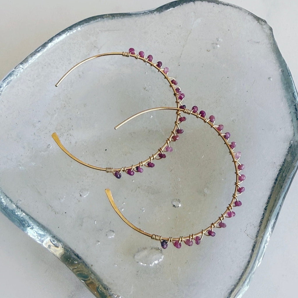 Gold hoop earrings with pink gemstones on a clear stone surface