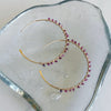Gold hoop earrings with pink gemstones on a clear stone surface