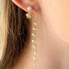 Close-up of a person wearing gold earrings with pearl-like beads.