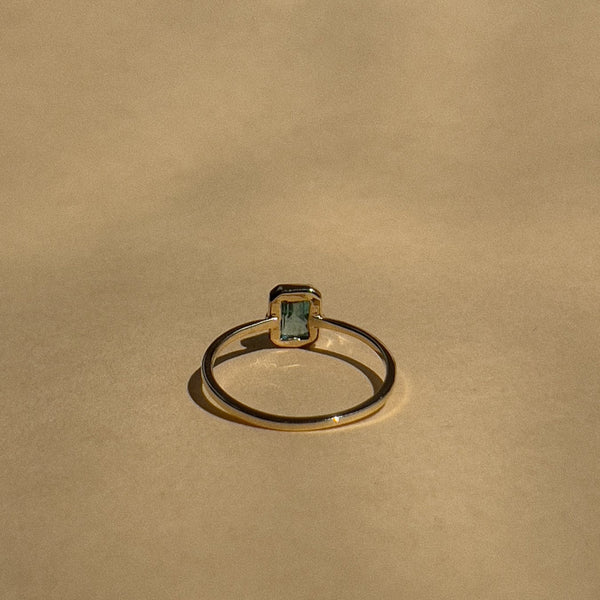 Gold ring with a green gemstone on a beige background