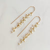 Pair of gold and pearl drop earrings on a light gray background