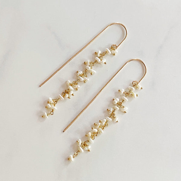 Pair of gold and pearl drop earrings on a light gray background