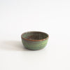 Small ceramic bowl with green speckly glaze and a small bit of the original brown clay color poking through the edge of the rim.
