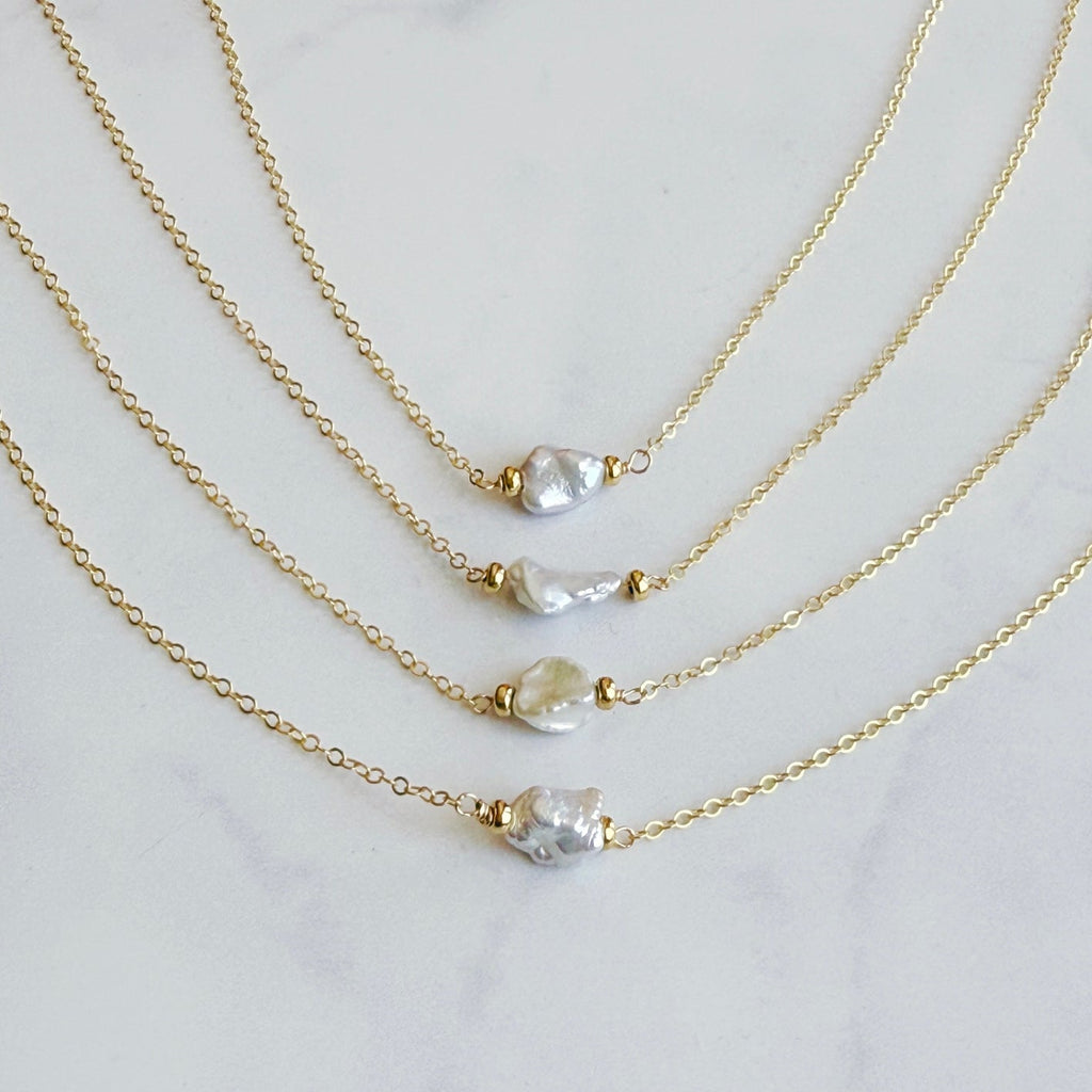 Three gold necklaces with variously shaped pearls on a light gray background