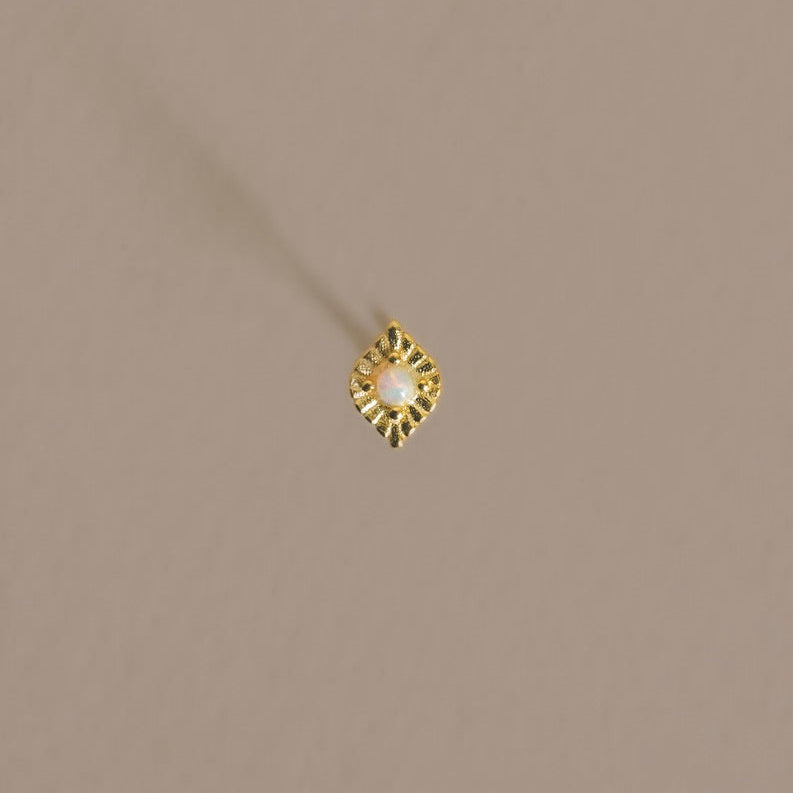 Gold earring with a central gemstone on a beige background