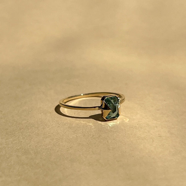 Gold ring with a green gemstone on a beige background