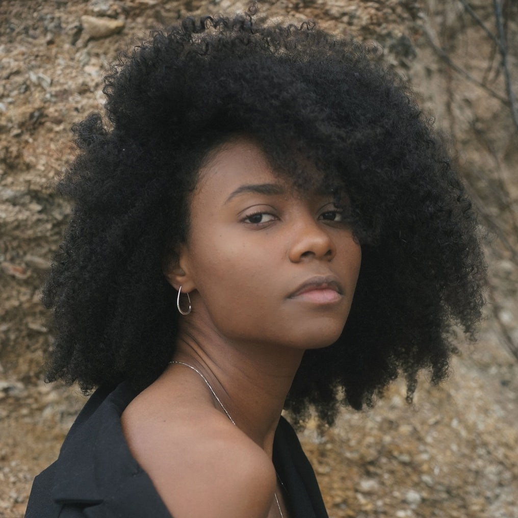 Woman with an afro wearing a black top against a natural background