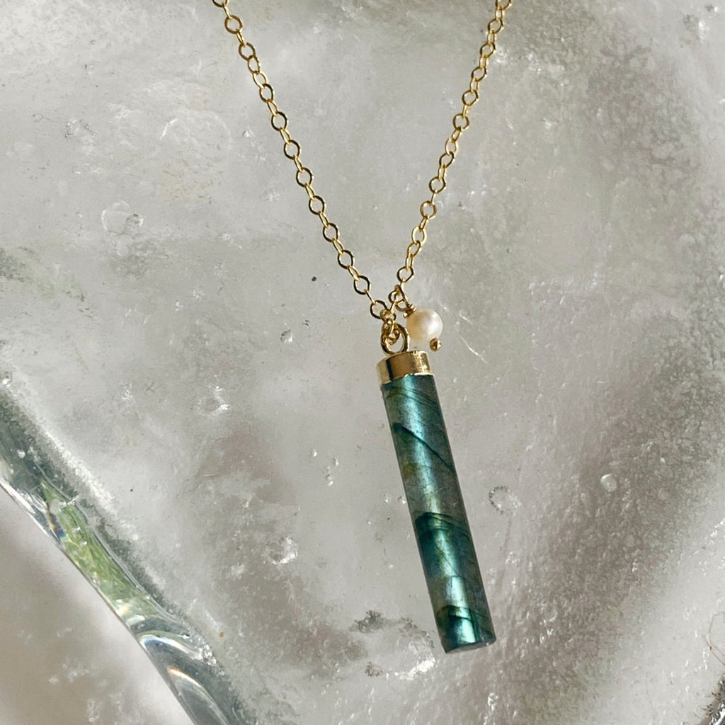 Necklace with a green cylindrical pendant on a textured stone background