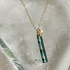 Necklace with a green cylindrical pendant on a textured stone background