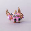 Decorative pink object with gold wings and embellishments on a light gray background