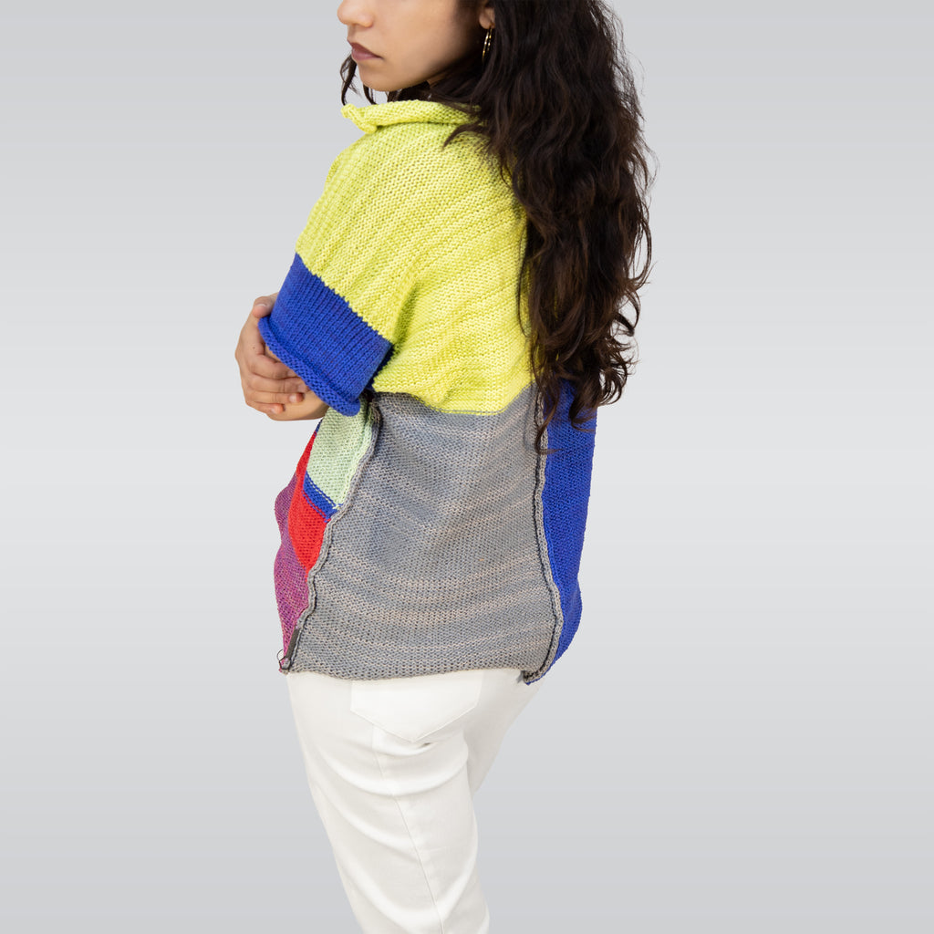 Person wearing a colorful striped sweater and white pants on a plain background