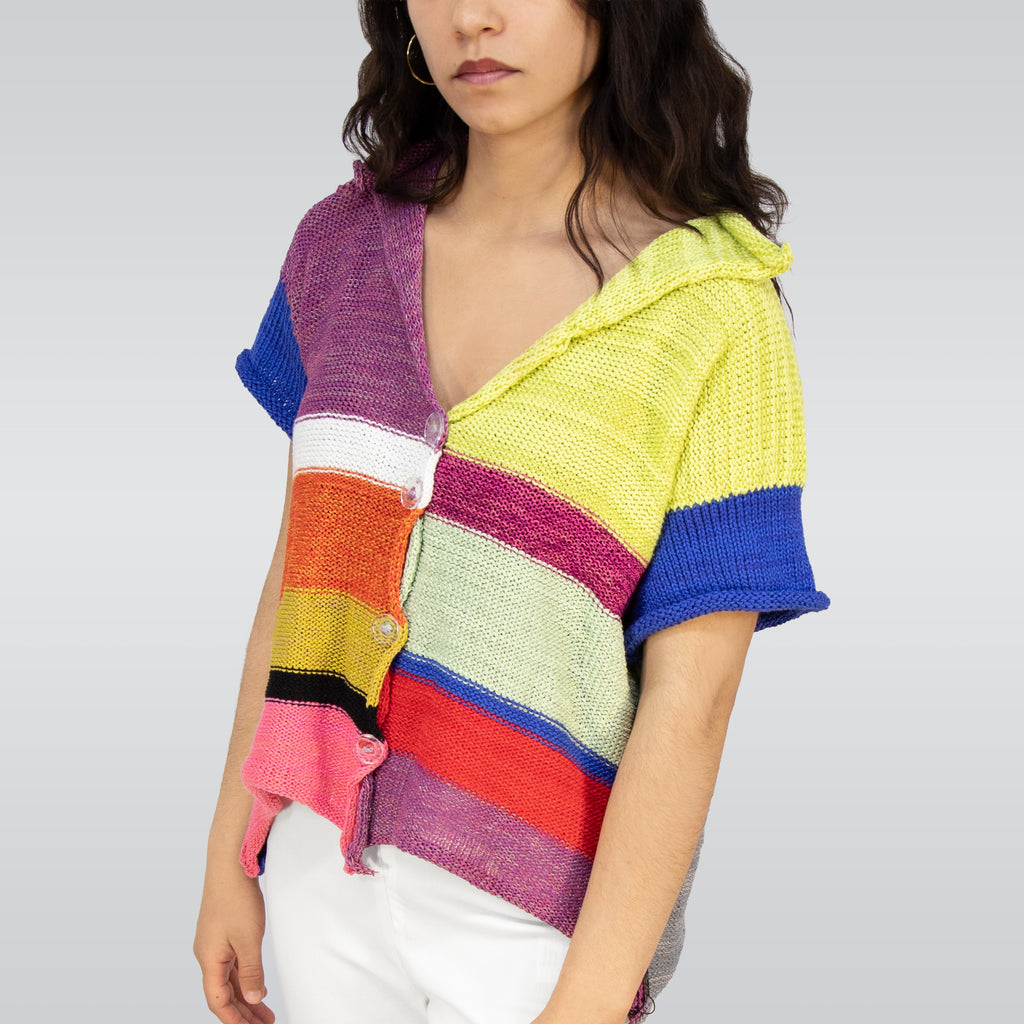 Person wearing a colorful striped sweater and white pants on a plain background