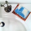 Bar of soap on a wooden soap dish next to a faucet labeled 'Cold' on a white sink.