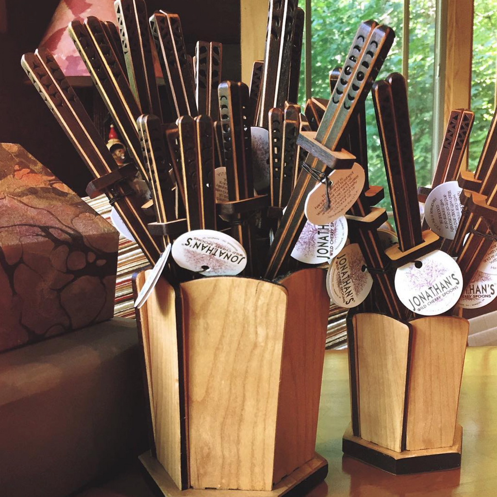 Two wooden display stands holding multiple chopsticks, with round white tags reading 'JONATHAN'S' attached. The scene is indoors near a window with greenery visible outside, and furniture is partially visible at the left edge.