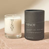 Two candles, one glass and one in black packaging, with 'MINOT' branding on a beige surface.