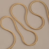 A gold snake chain necklace draped in an S-shaped loop on a neutral beige background.