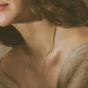 A close-up lifestyle shot of a model wearing a delicate, thin gold chain necklace and a beige knit sweater.