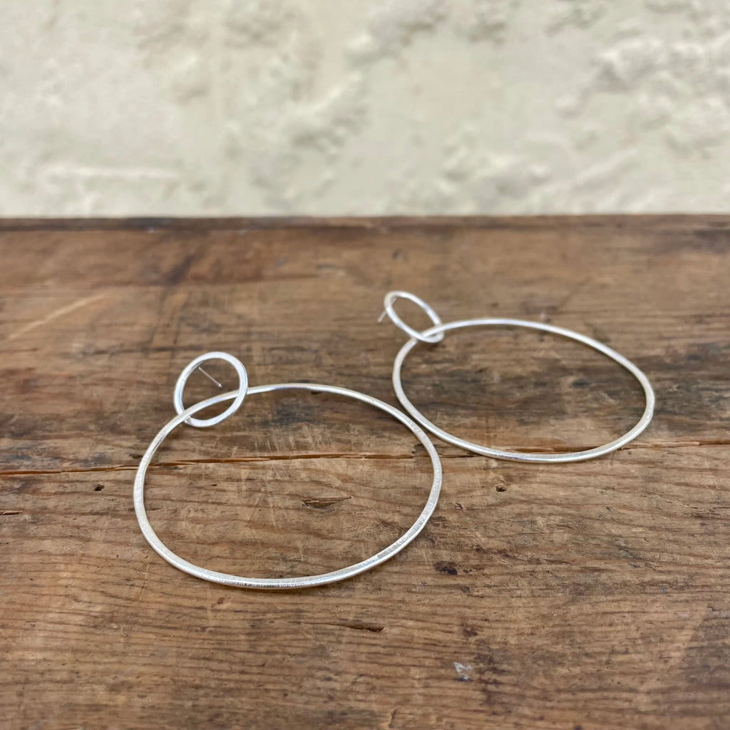 Silver hoop earrings on a wooden surface with a neutral background
