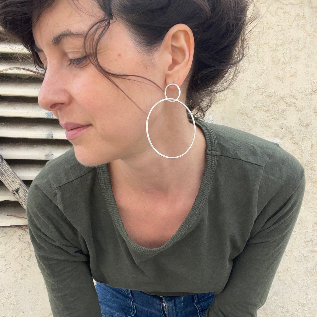 Woman wearing large hoop earrings and a green long-sleeve shirt against a neutral background