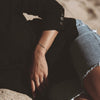 Person wearing a black shirt and denim shorts sitting on sand