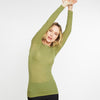 Woman wearing a green long-sleeve top with arms raised against a white background