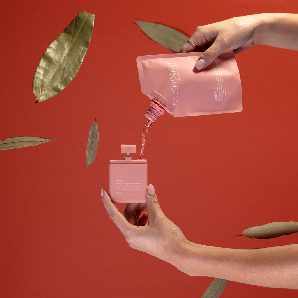 Person pouring liquid from a pink pouch into a small pink bottle against a red background with leaves.