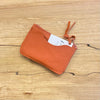 Orange leather cardholder with a tag on a wooden surface
