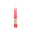 A pair of tall, slender pink taper candles standing upright side by side, wrapped together with a cream paper band featuring a bee logo and a gold glitter accent, isolated on a white background.