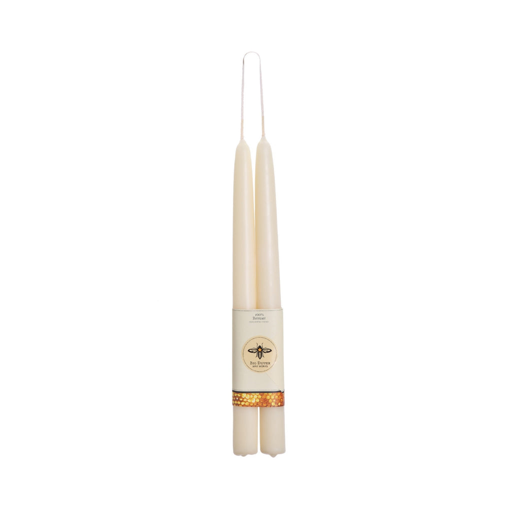 A pair of cream taper candles in a double-wick holder with a paper label band featuring a bee logo and gold pattern, isolated on a white background.