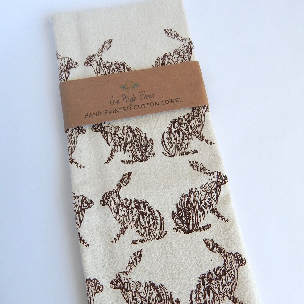 White towel with brown rabbit pattern and 'The High Fiber' label on a light blue background