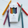A set of five colorful tapers candles, each dipped in wax and placed on a white surface, with a box labeled 'TAPER CANDLES' in the background.