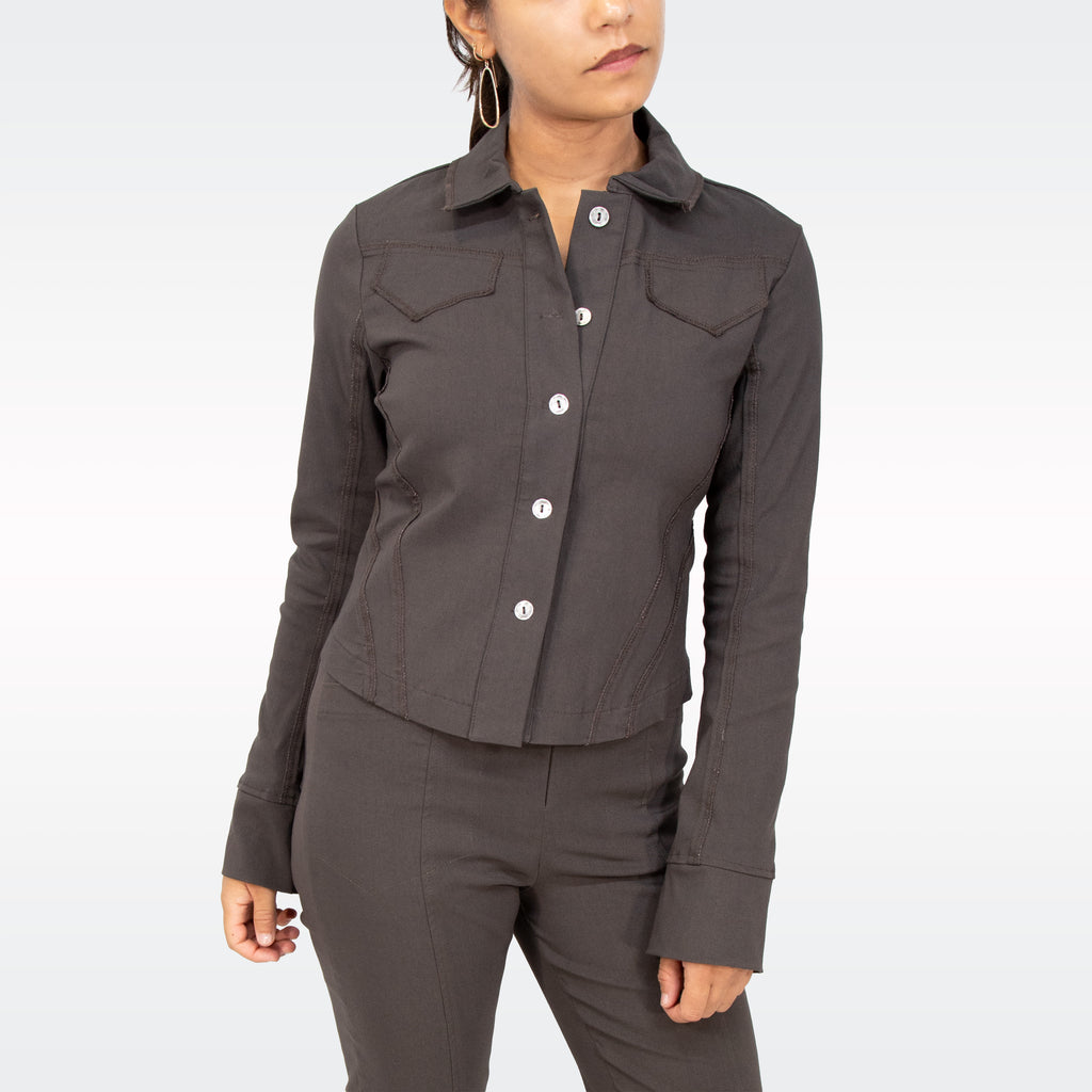 A woman wearing a dark brown cropped button-up shirt with chest pockets and matching dark brown pants, shown against a light gray studio background.