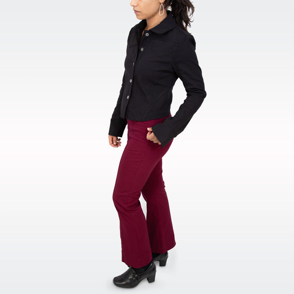 A woman modeling a black button-front jacket and burgundy flared pants against a clean white studio background.