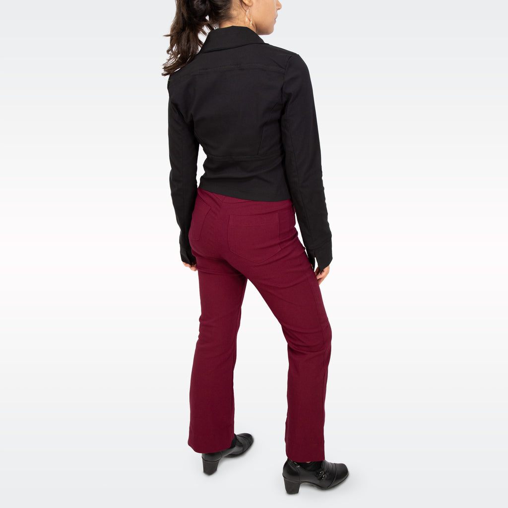 A woman shown from the back wearing a black long-sleeve collared shirt and burgundy straight-leg pants, paired with black heeled shoes, against a light gray studio background.