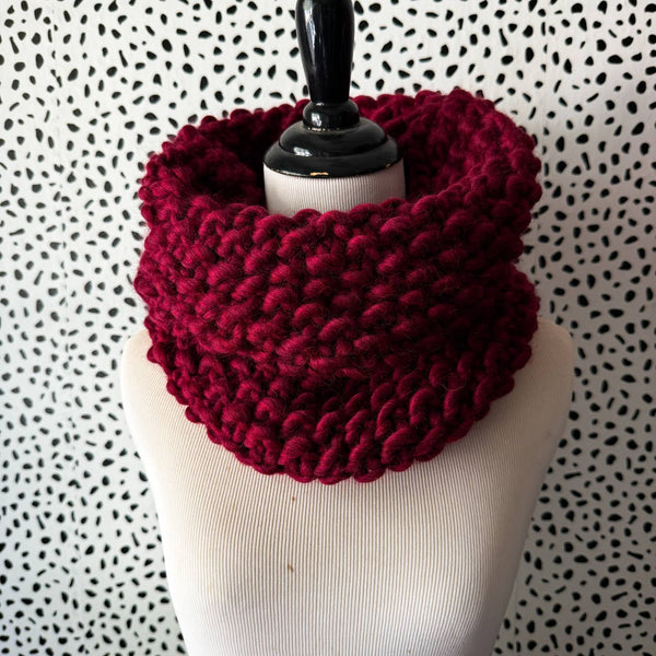 Red knitted cowl on a mannequin against a patterned background