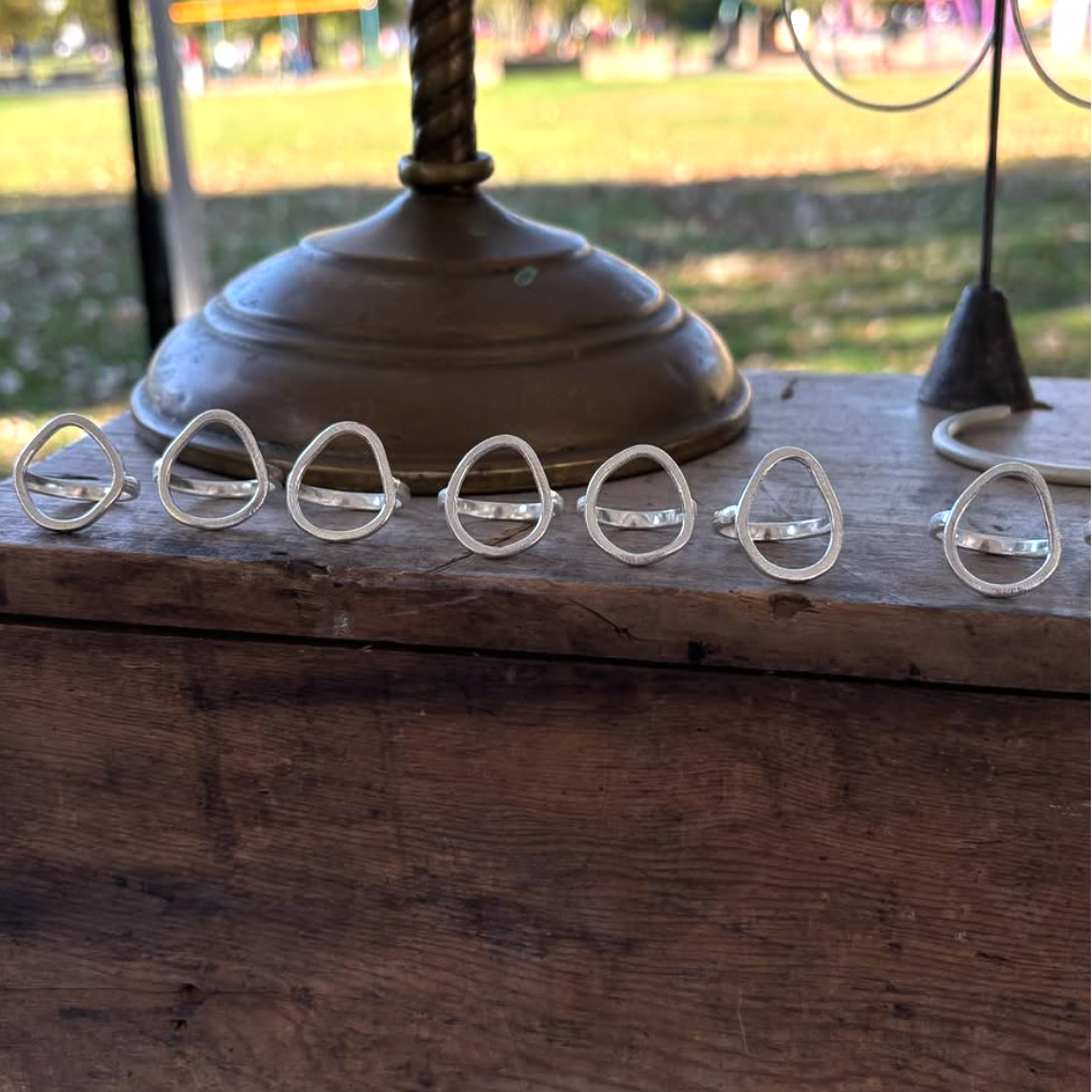 Set of silver rings on a wooden surface with a blurred outdoor background