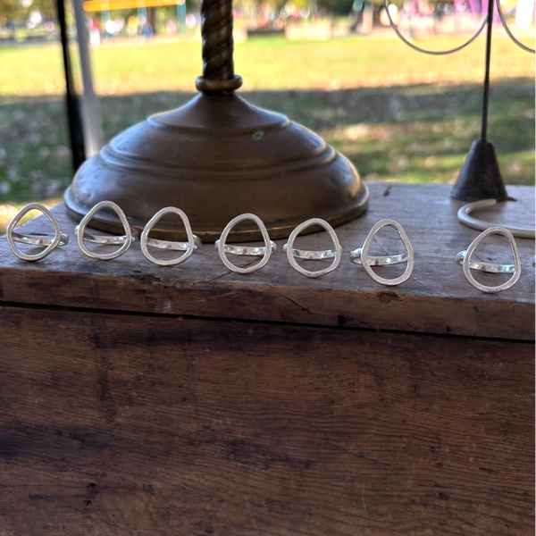 Set of silver rings on a wooden surface with a blurred outdoor background