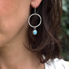 Close-up of a woman wearing silver hoop earrings with a small round gemstone.