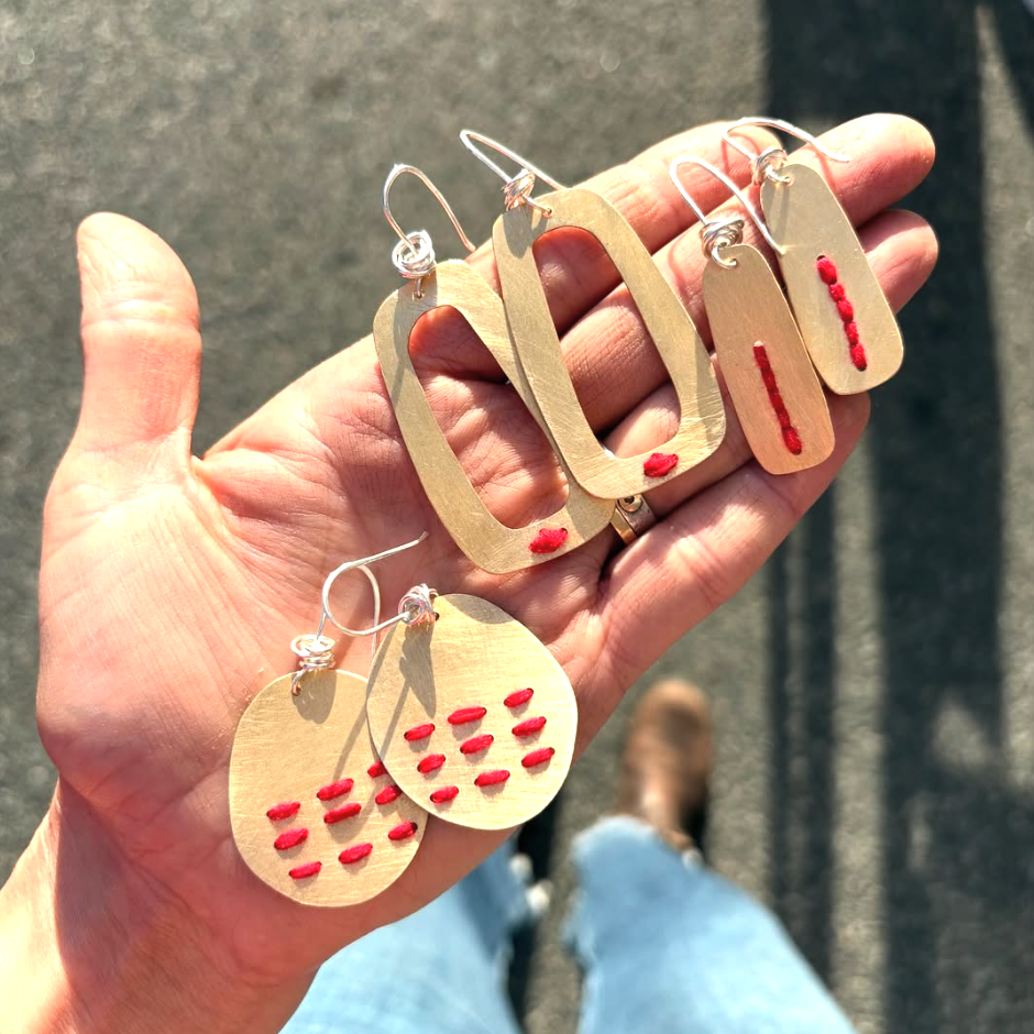 Hand holding gold and red earrings against a blurred background