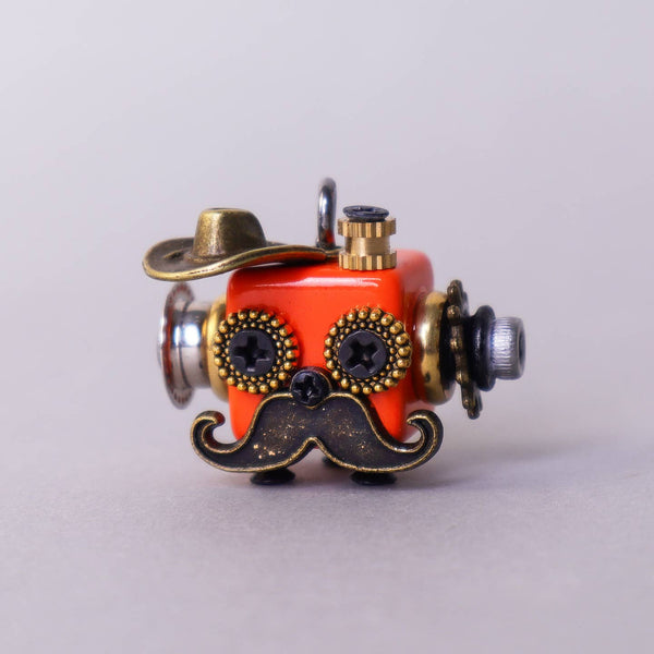 Small mechanical object with a red face, gold accents, and a mustache on a light gray background