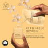 A hand holds a Noshinku refillable hand sanitizer spray pouch while pouring liquid into a matching vanilla cream bottle, with a second hand holding the pouch. White orchid flowers float around the product on a warm beige background, with text reading 'REFILLABLE DESIGN' and 'Say goodbye to single use plastic.